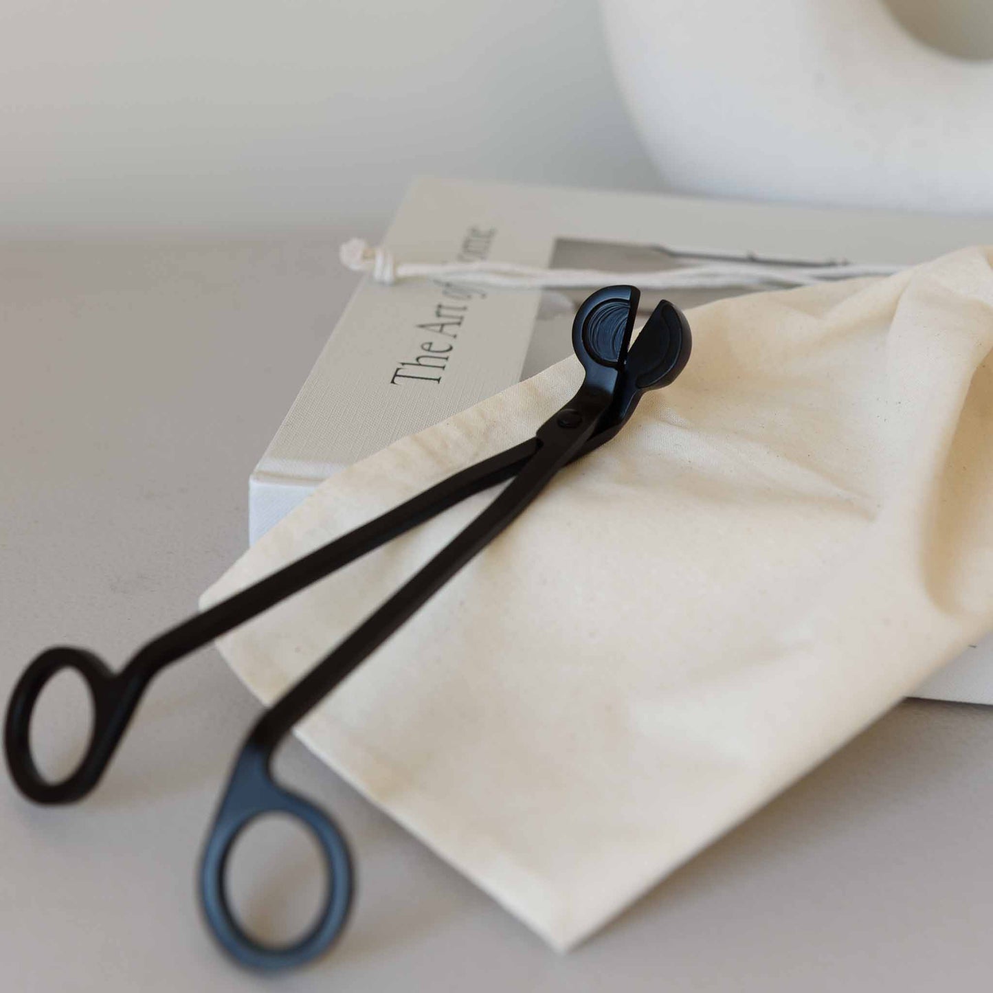 Black metal wick trimmer placed inside a reusable bag, ideal for candle care and maintenance.