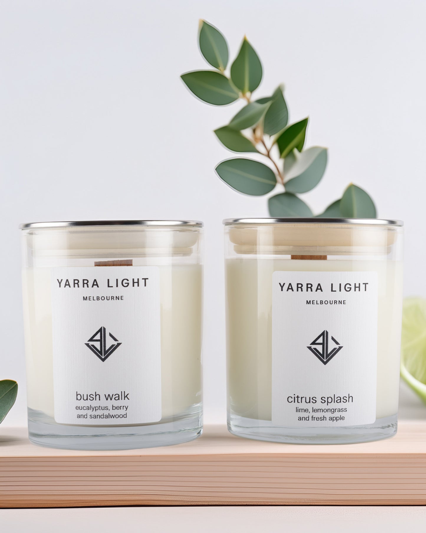 Two Yarra Light soy wax candles on a wooden surface with a plant in the background.