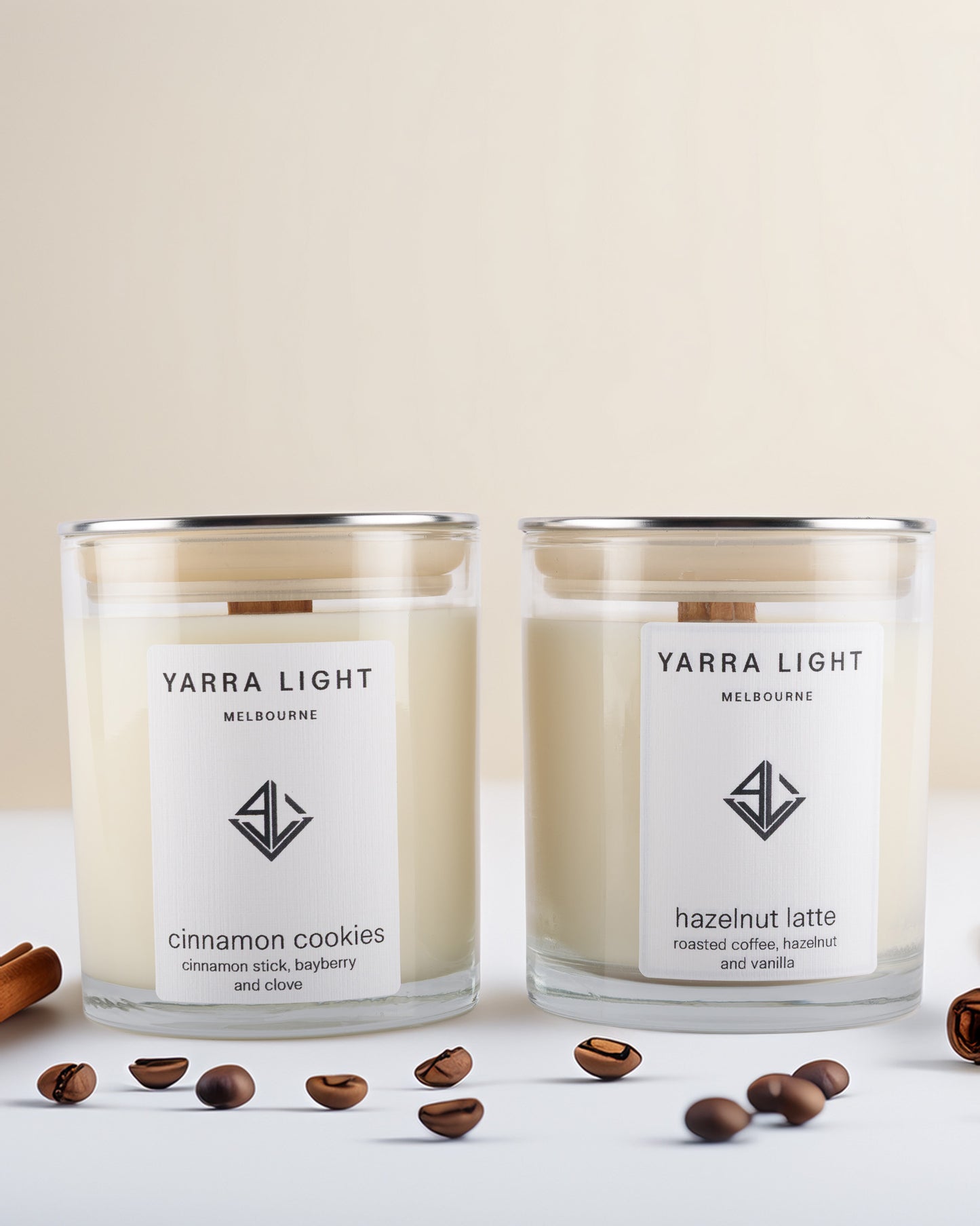 Two Yarra Light soy wax candles on a light background with coffee beans and cinnamon sticks.