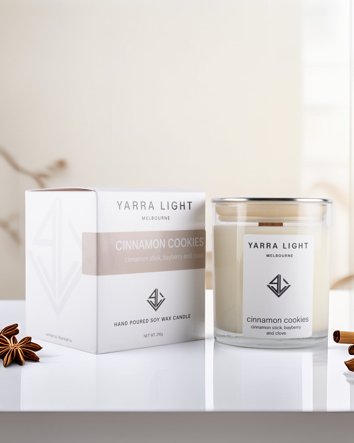 Yarra Light cinnamon cookies soy wax candle and packaging on a white surface with cinnamon sticks.