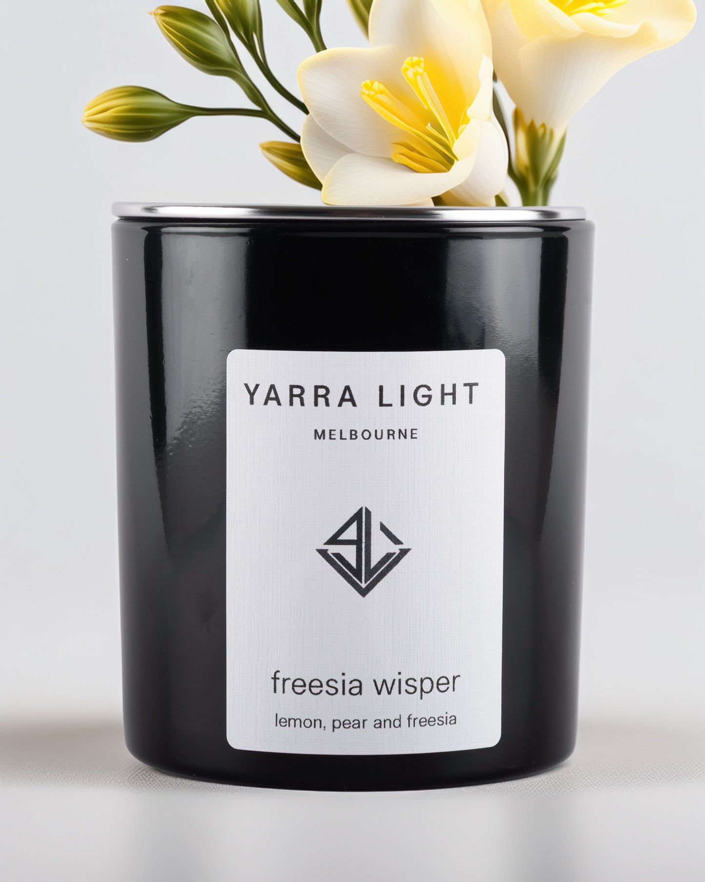 Black glossy candle with 'Yarra Light Melbourne' label and freesia flowers on a light background