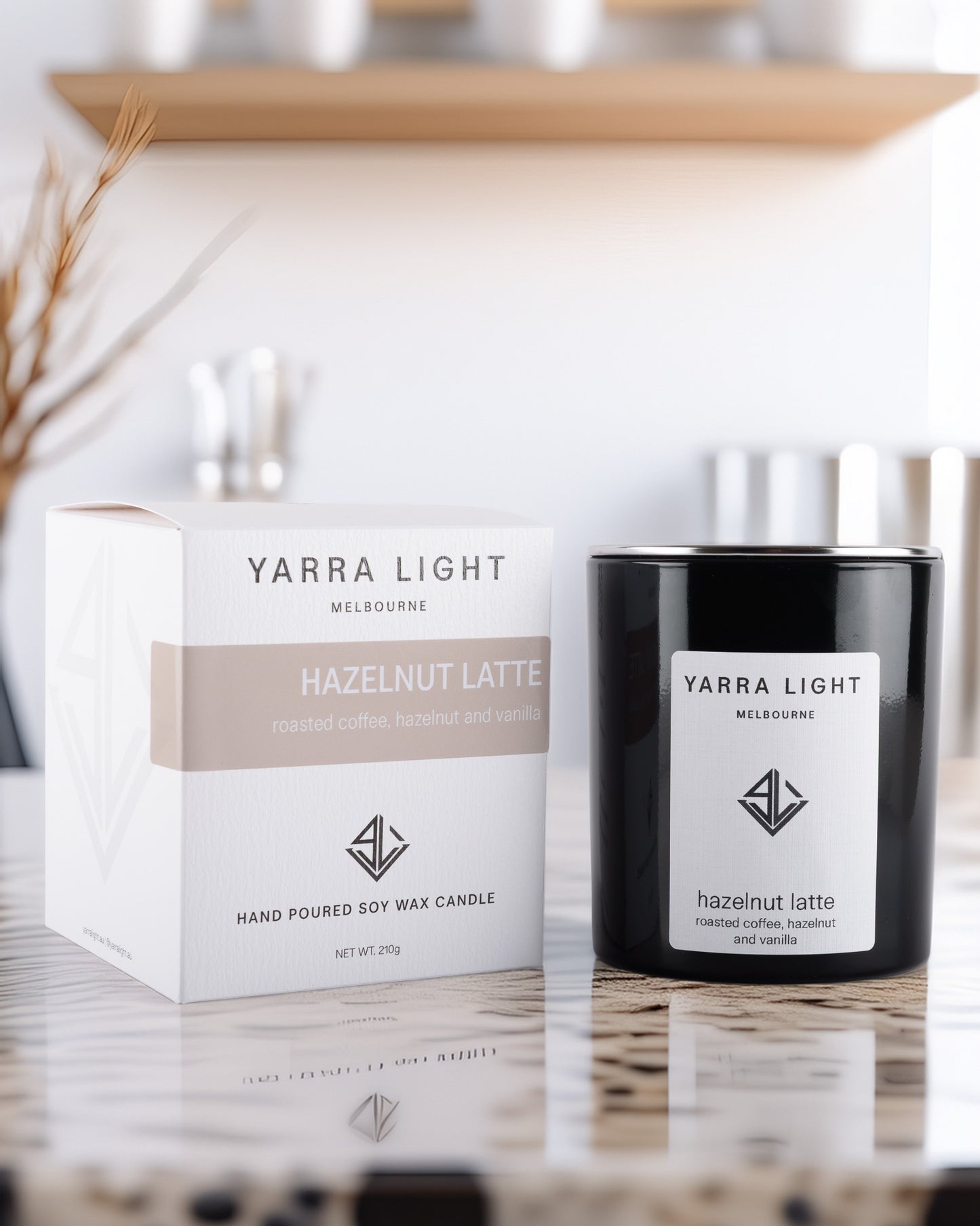 Yarra Light Hazelnut Latte soy wax candle and packaging on a reflective surface with a blurred background