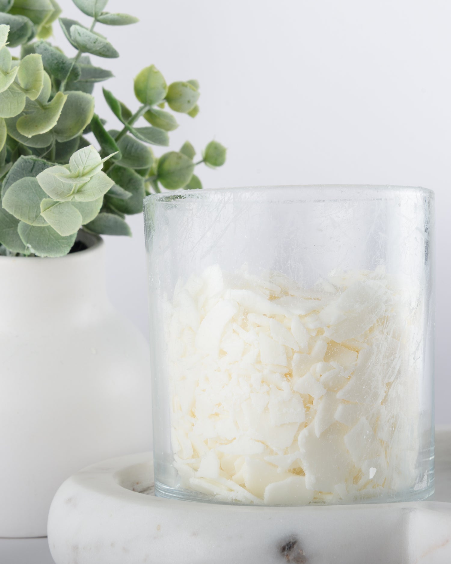 Glass candle jar with white natural soy wax next on a light background