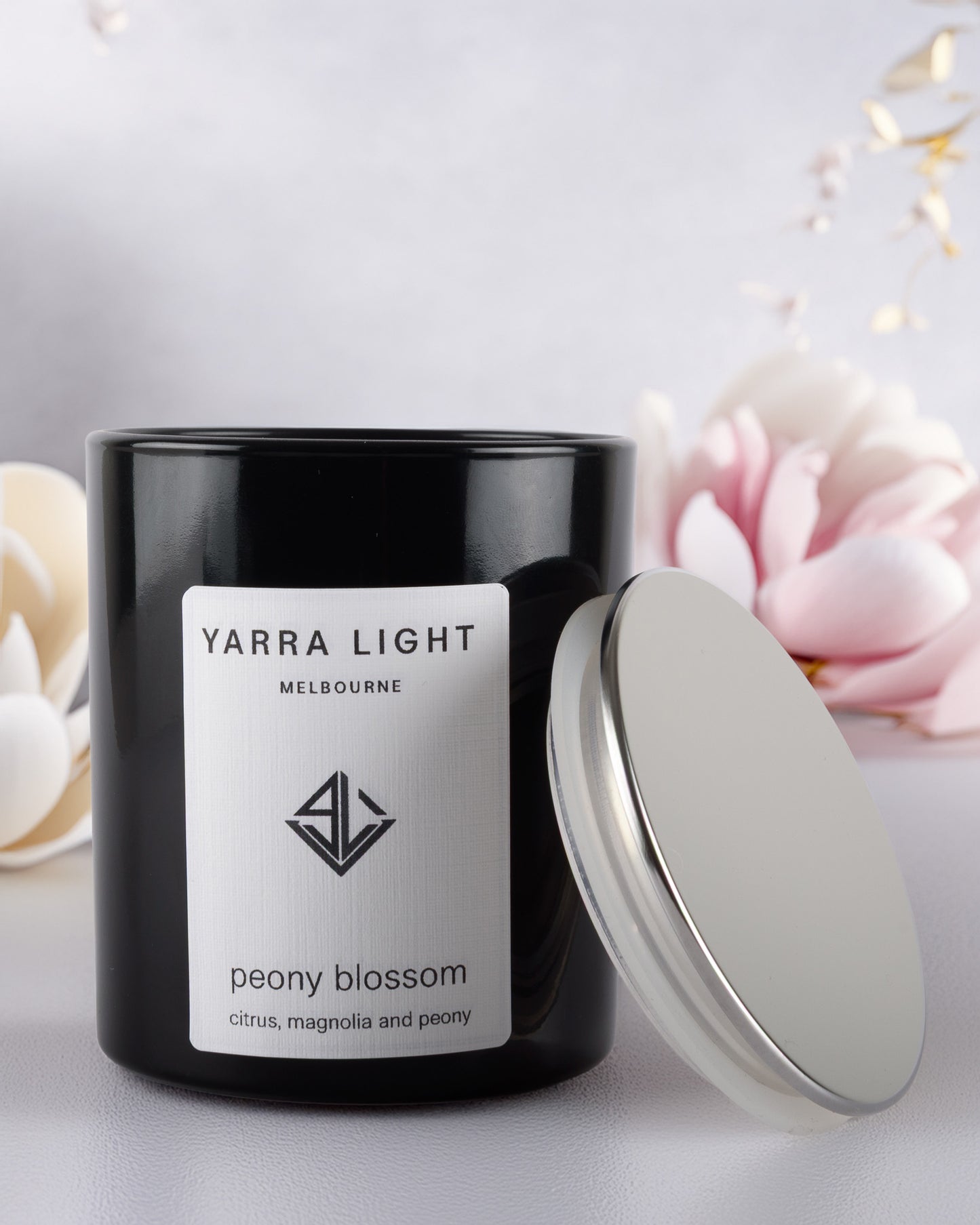 Black glossy candle with a white label featuring 'Yarra Light' on a light background with peony flowers.
