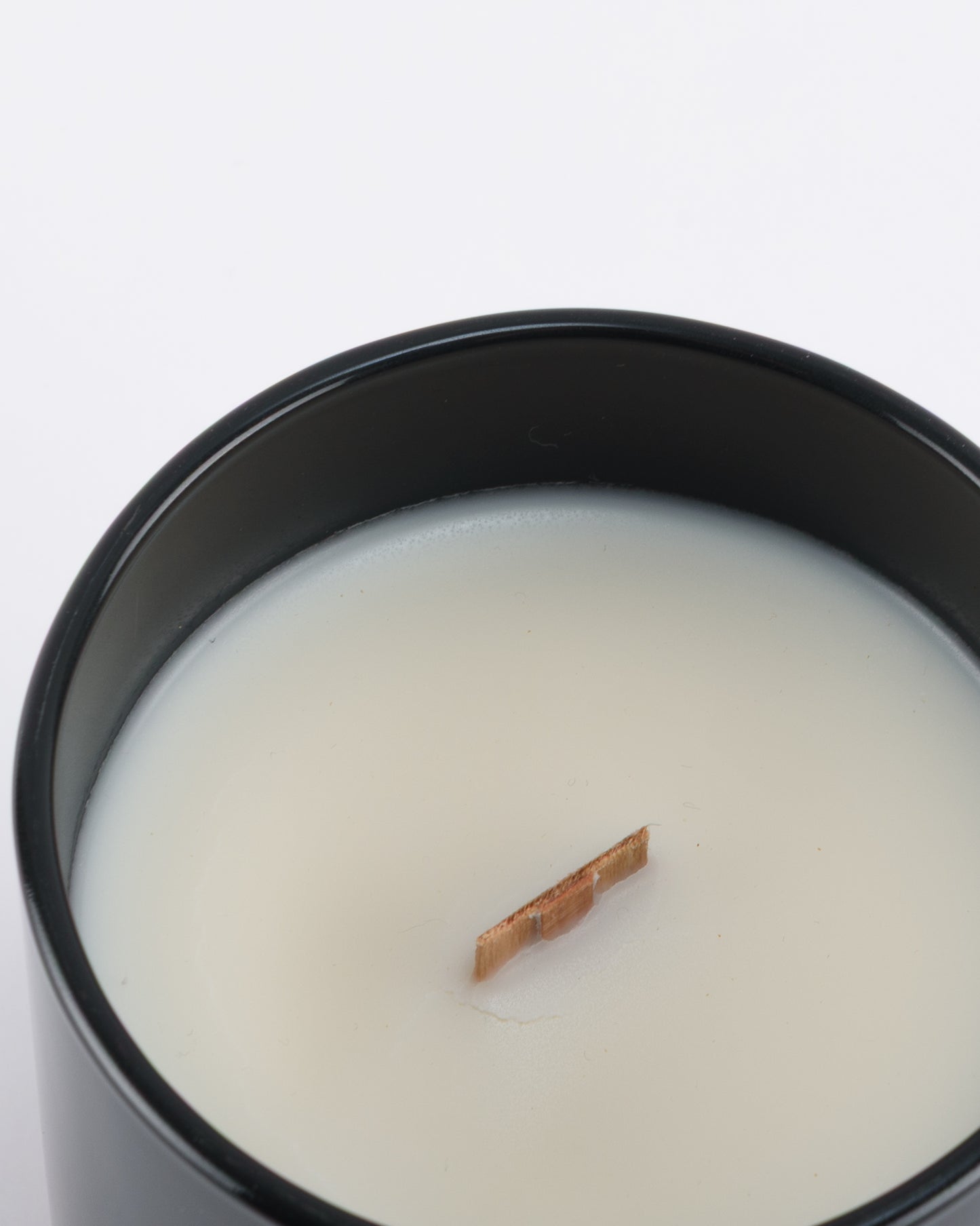 NOIR soy wax scented candle with wood wick in a black glossy glass jar.