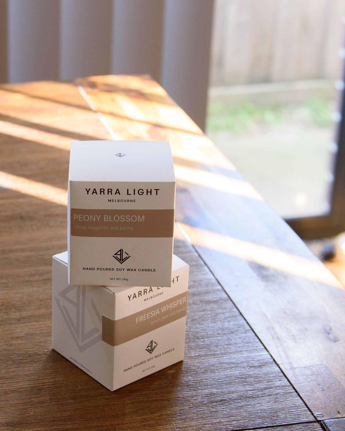 Two Yarra Light candle boxes, resting on a natural wooden surface with soft lighting highlighting their minimalist design.