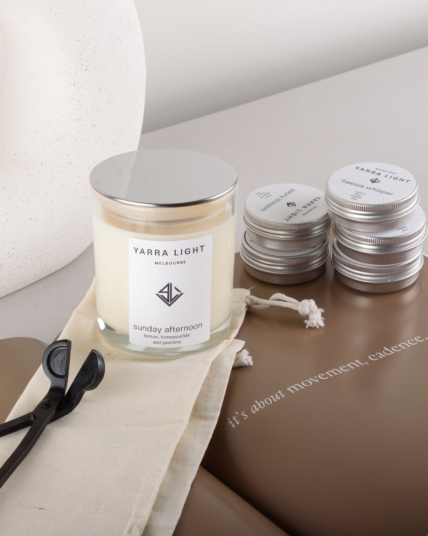 Yarra Light soy wax candle, sample candle tins and wick trimmer on a surface with a neutral background
