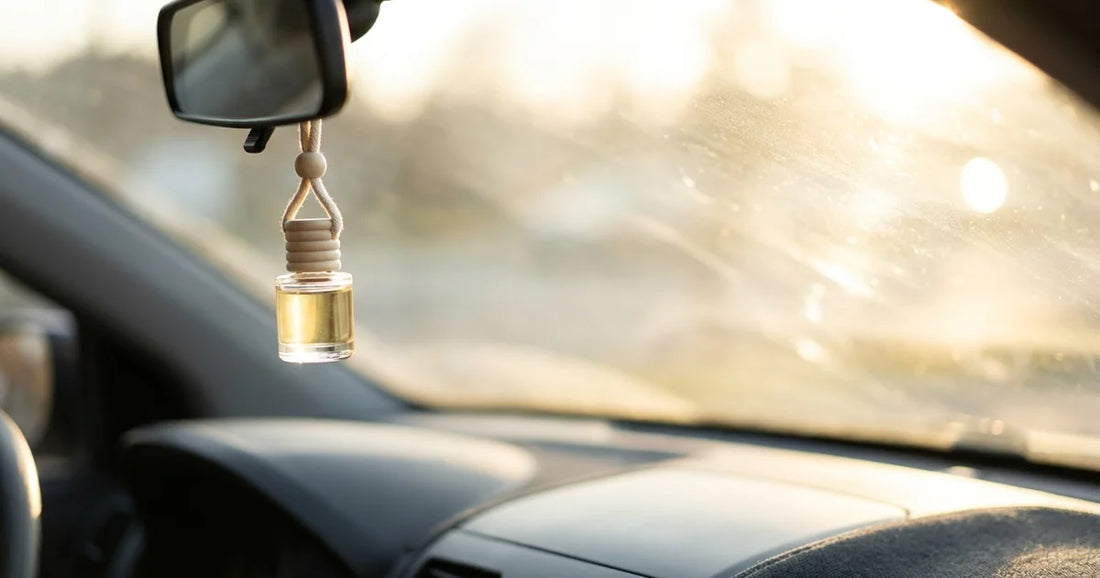 A small glass car diffuser bottle with a timber cap hanging from a rear-view mirror in warm afternoon sun