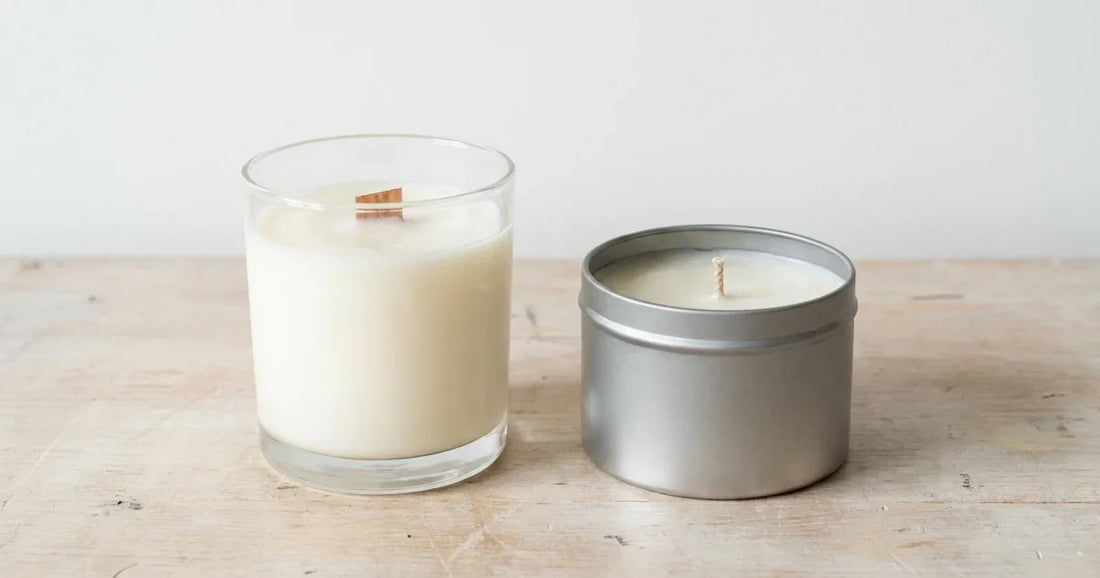 Two soy candles side by side on a bench, one in clear glass and one in a metal tin, unlit