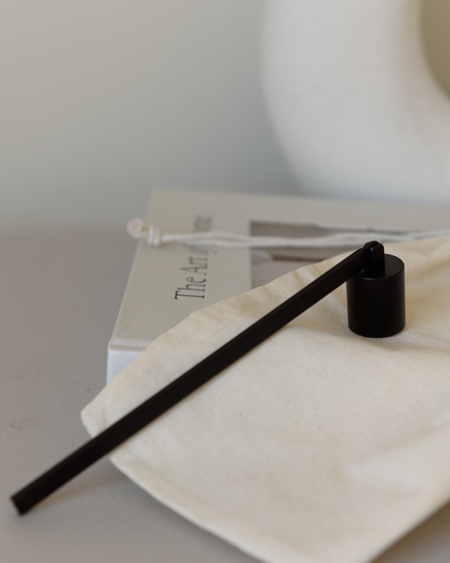Black metal candle snuffer placed inside a reusable bag, ideal for safe candle extinguishing and maintenance