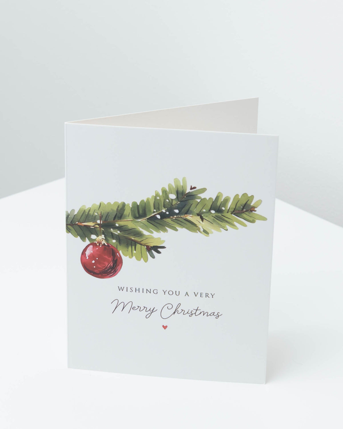 Christmas card with a green pine branch and a red bauble, reading Wishing you a very Merry Christmas