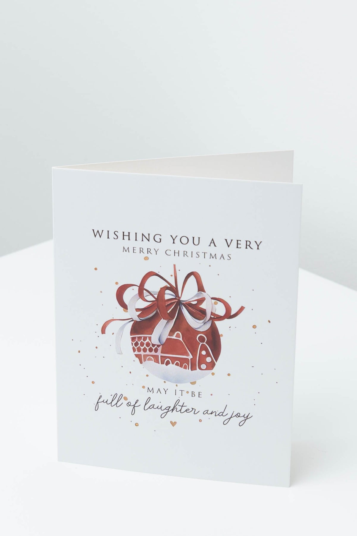 Christmas card with a red bauble tied with a ribbon bow, reading Wishing you a very Merry Christmas, may it be full of laughter and joy