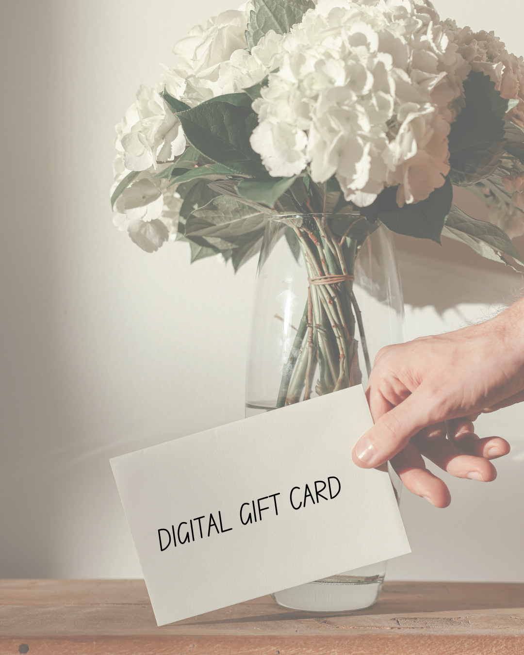 Digital gift card held by a hand with a vase of white flowers in the background