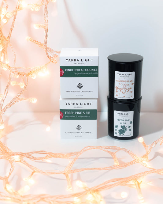 Gingerbread Cookies and Fresh Pine & Fir Christmas soy candles in black glass jars, stacked beside their white gift boxes with fairy lights