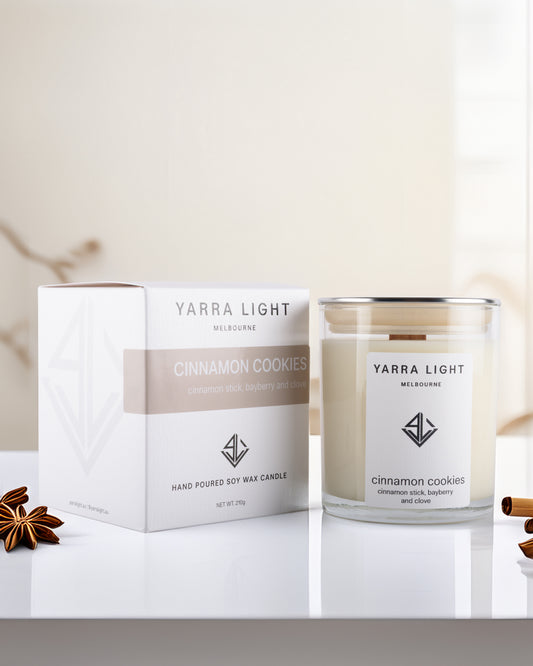Yarra Light cinnamon cookies soy wax candle and packaging on a white surface with cinnamon sticks.
