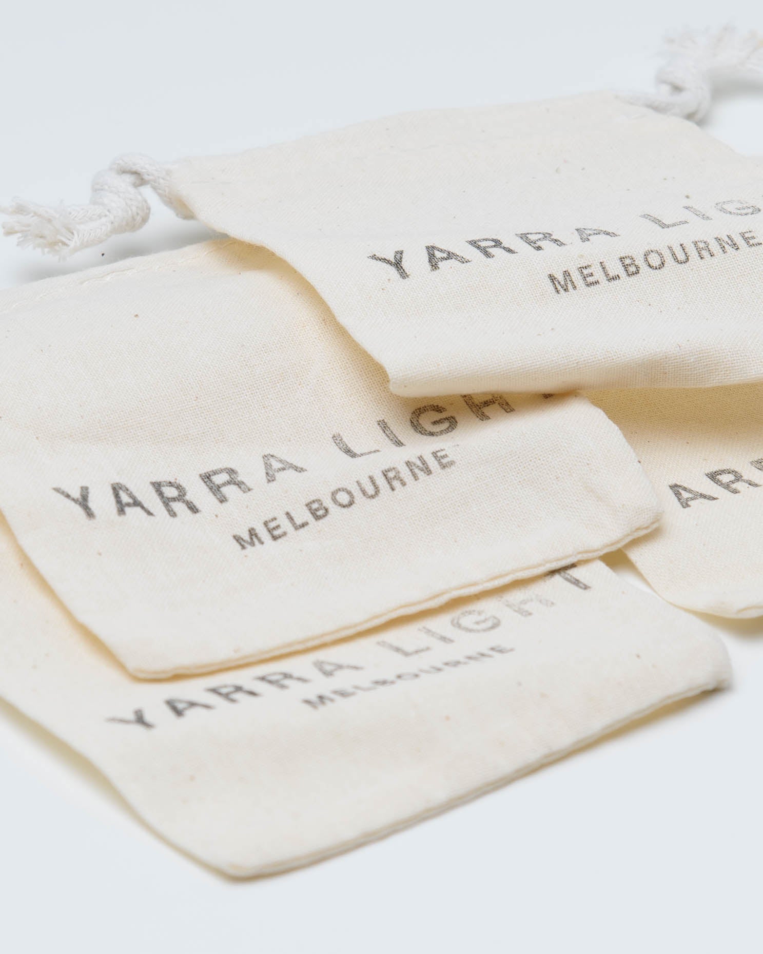 Four small cream-colored fabric drawstring pouches stacked on a white background, each printed with the text 'YARRA LIGHT MELBOURNE' in a dark gray serif font.