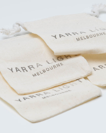 Four small cream-colored fabric drawstring pouches stacked on a white background, each printed with the text 'YARRA LIGHT MELBOURNE' in a dark gray serif font.