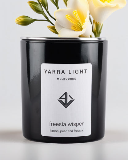 Black glossy candle with 'Yarra Light Melbourne' label and freesia flowers on a light background