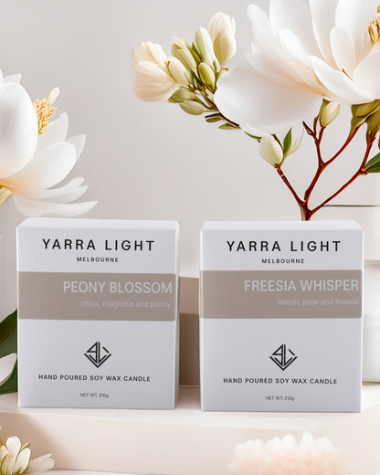 Two Yarra Light candles in boxes with flowers in the background