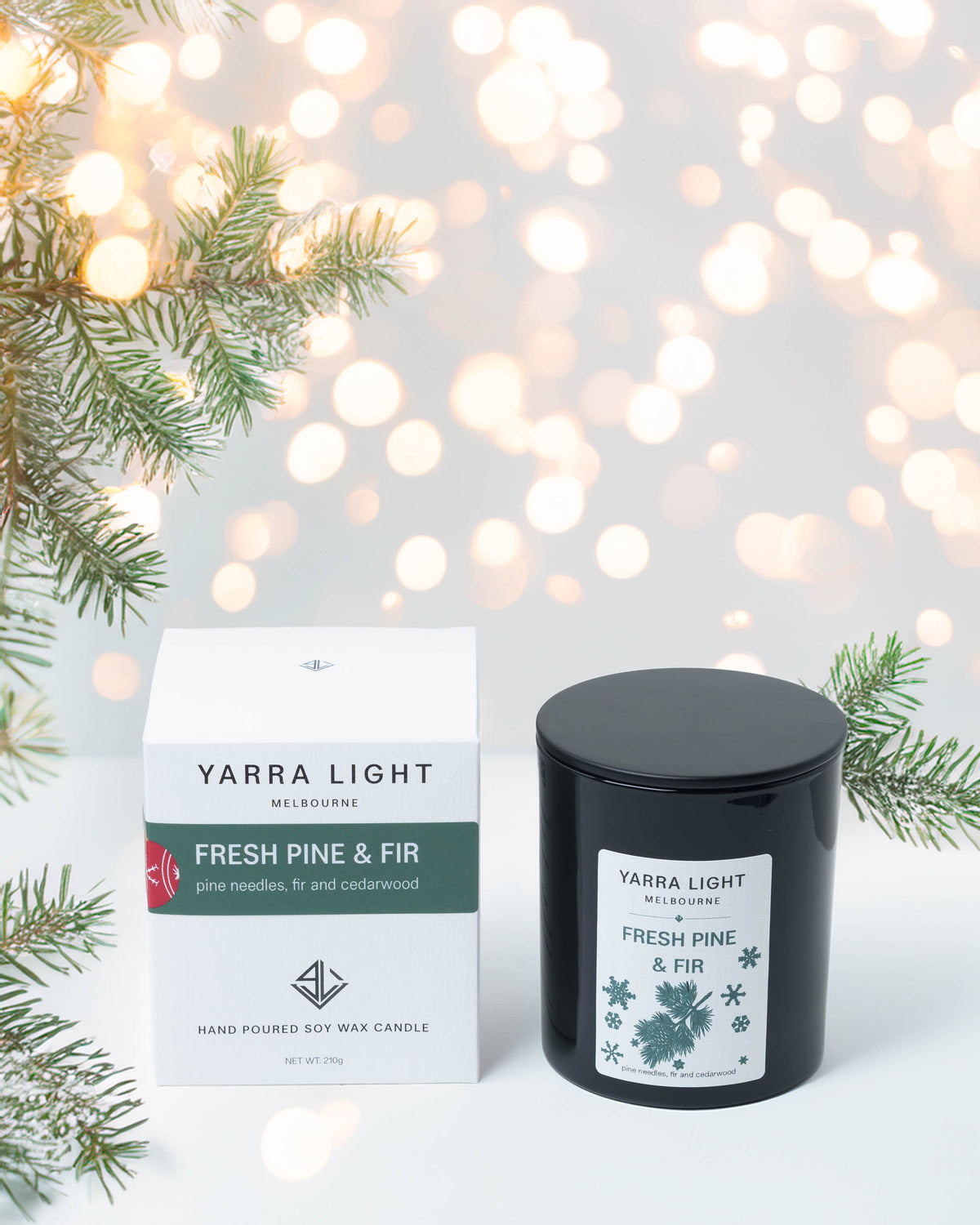 Fresh Pine & Fir Christmas soy candle in a black glass jar beside its gift box, with pine branches and fairy lights