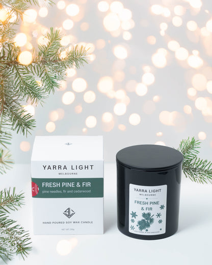 Fresh Pine & Fir Christmas soy candle in a black glass jar beside its gift box, with pine branches and fairy lights