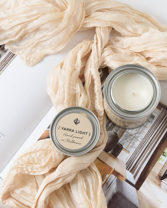 Two candles with 'Yarra Light' branding on a beige scarf and magazine