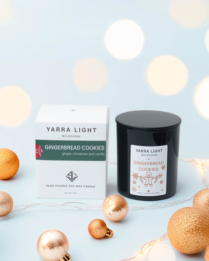 Gingerbread Cookies Christmas soy candle in a black glass jar beside its gift box, with copper baubles and fairy lights