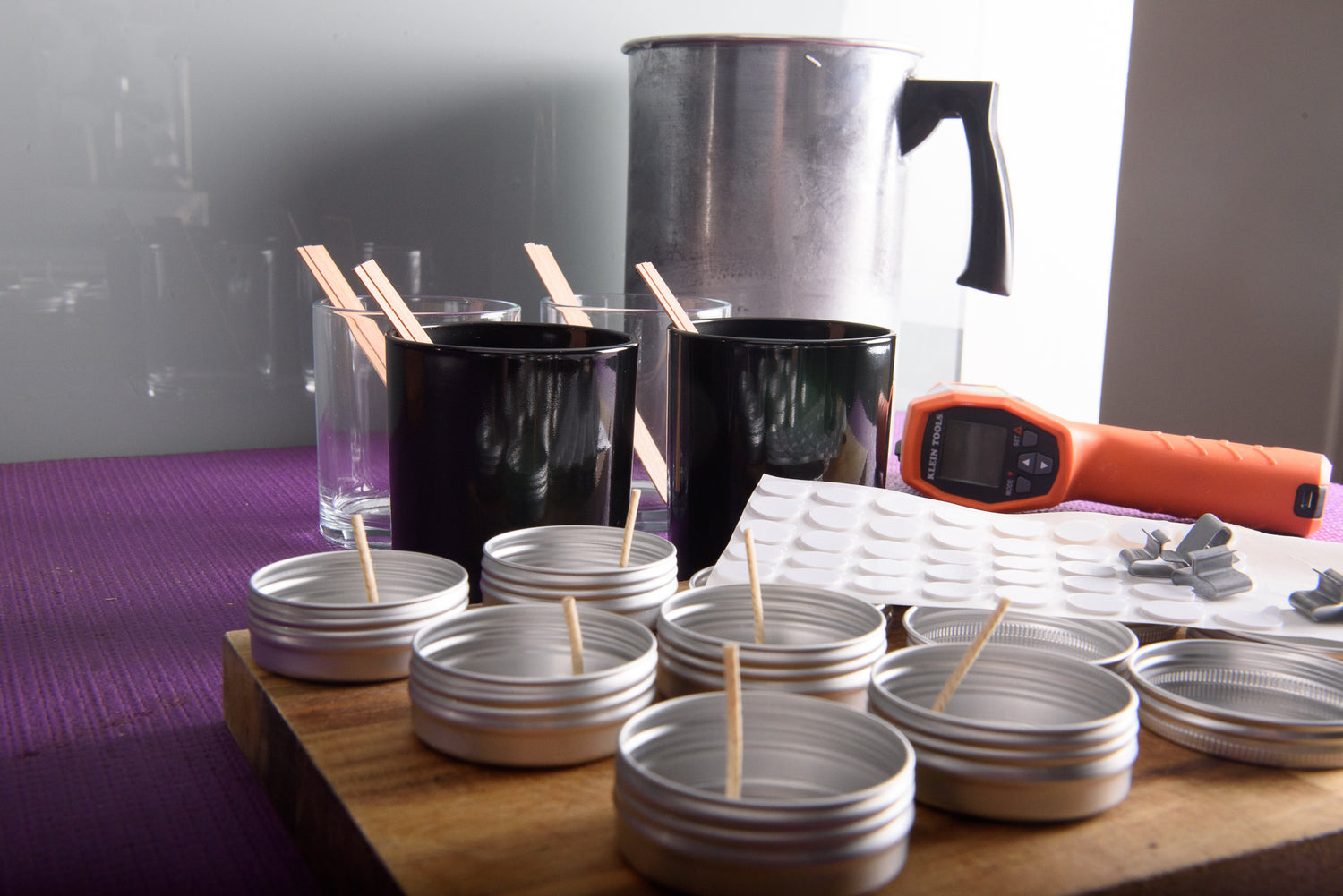 Candle-making setup with glass jars, wood wicks, and metal tins with cotton wicks on a wooden surface