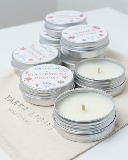 Open mini Christmas soy candle tins with cotton wicks beside lidded Gingerbread Cookies and Cinnamon Cookies tins