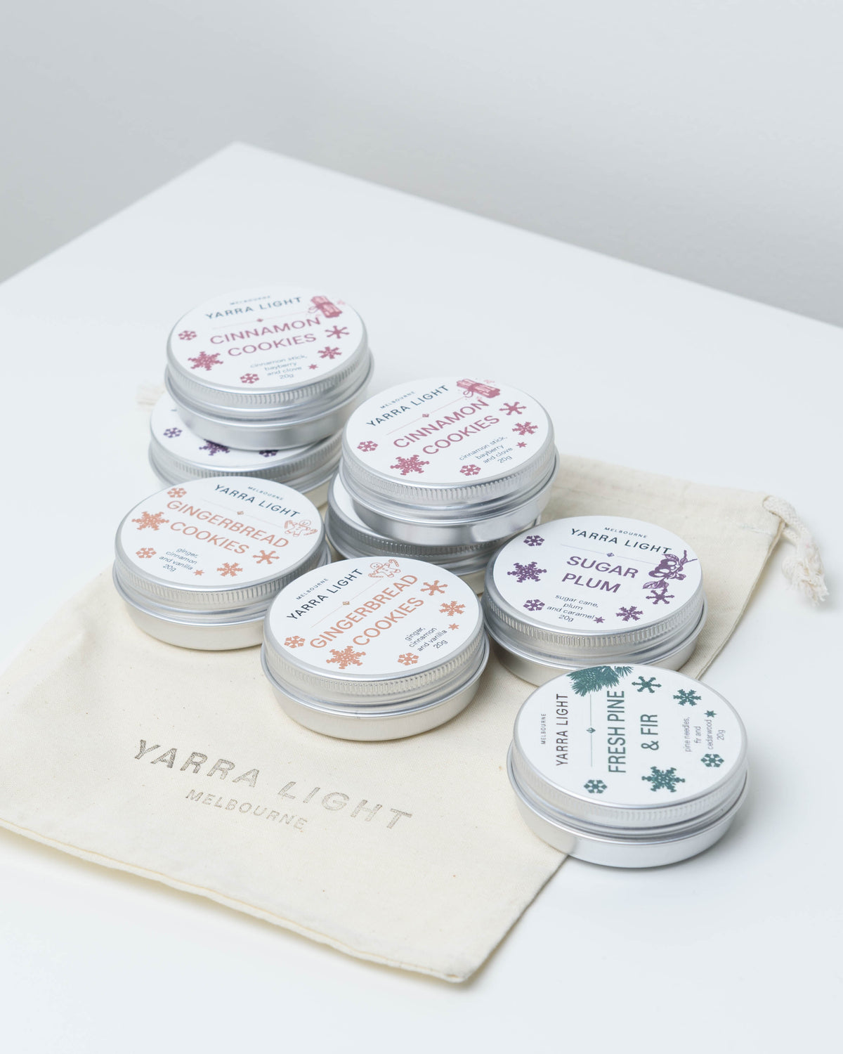 Eight mini Christmas soy candle tins: Cinnamon Cookies, Gingerbread Cookies, Sugar Plum and Fresh Pine & Fir on a Yarra Light cotton pouch