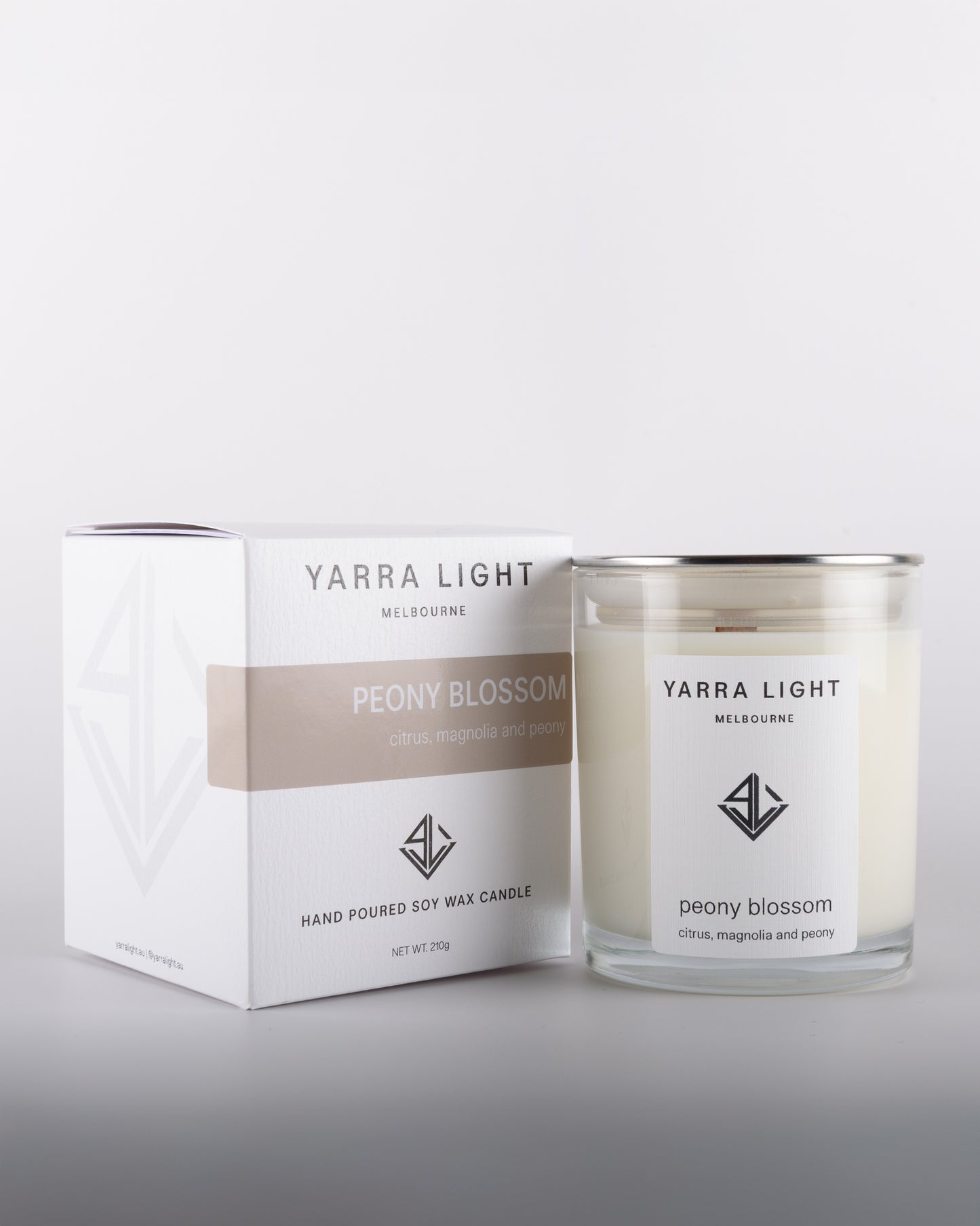Peony Blossom soy wax scented candle with wood wick in a clear glass jar with minimalist label, placed beside its eco-friendly packaging box in warm neutral tones, inspired by the delicate and romantic fragrance of blooming peonies.