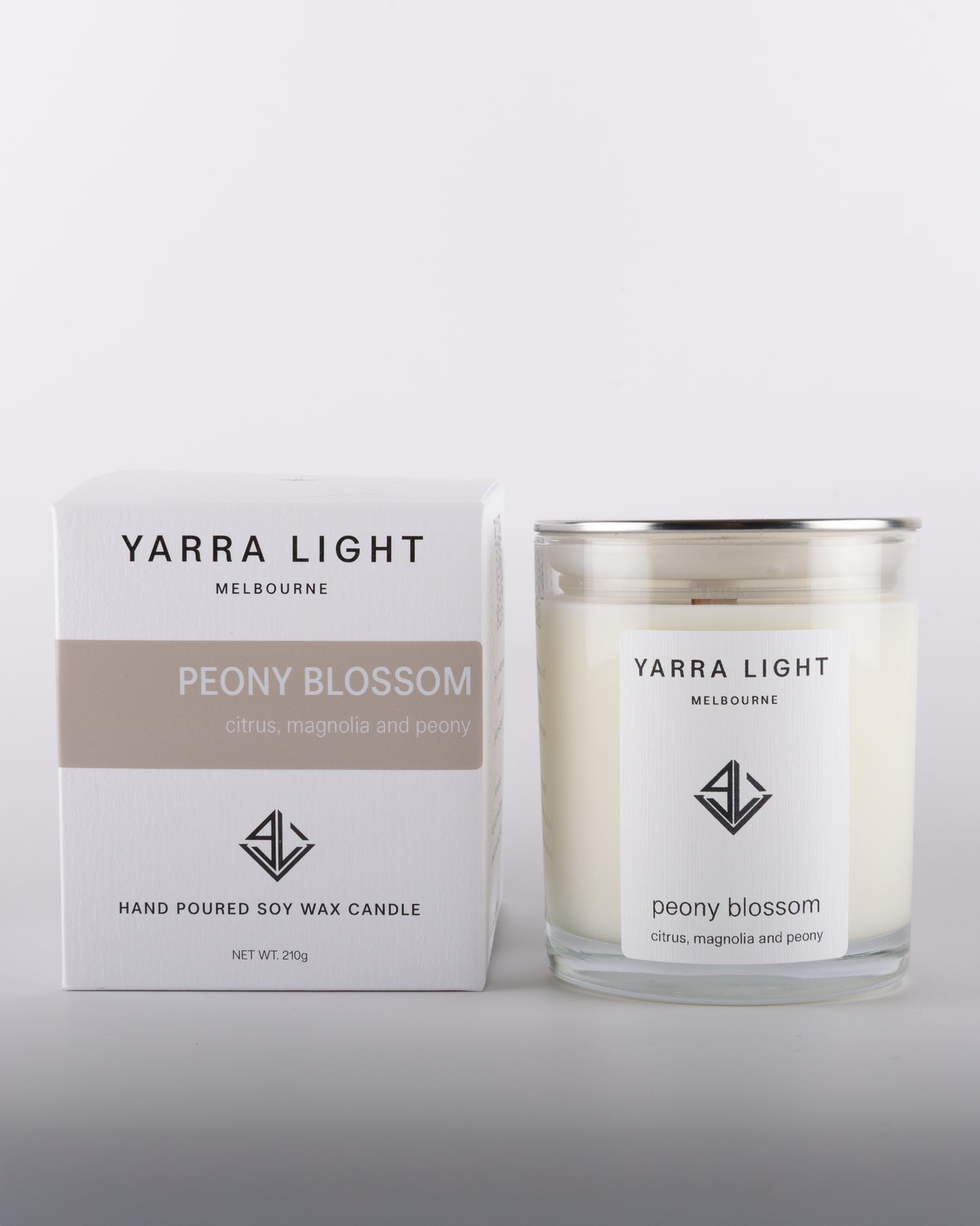 Peony Blossom soy wax scented candle with wood wick in a clear glass jar with minimalist label, placed beside its eco-friendly packaging box in warm neutral tones, inspired by the delicate and romantic fragrance of blooming peonies.