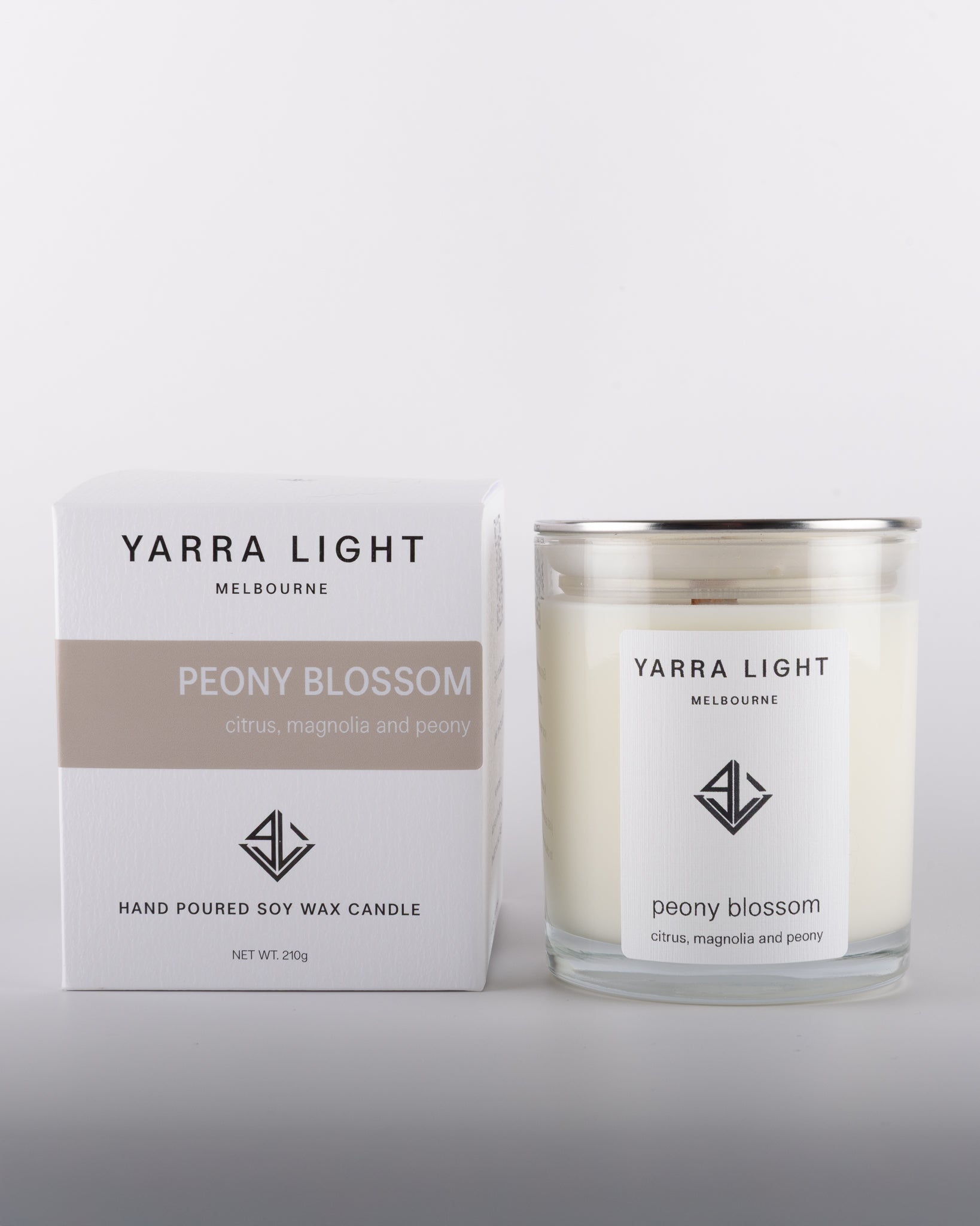 Peony Blossom soy wax scented candle with wood wick in a clear glass jar with minimalist label, placed beside its eco-friendly packaging box in warm neutral tones, inspired by the delicate and romantic fragrance of blooming peonies.