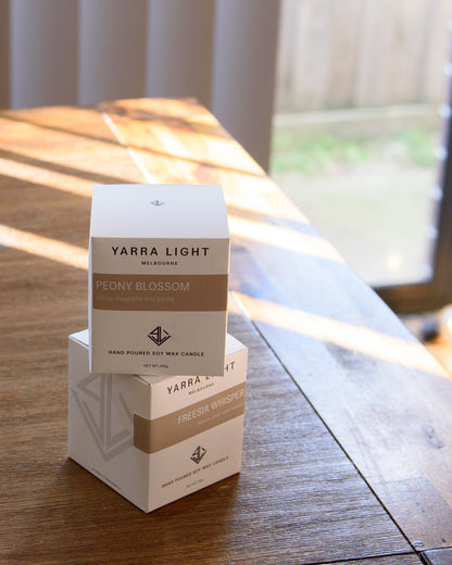 Two Yarra Light candle boxes, resting on a natural wooden surface with soft lighting highlighting their minimalist design.