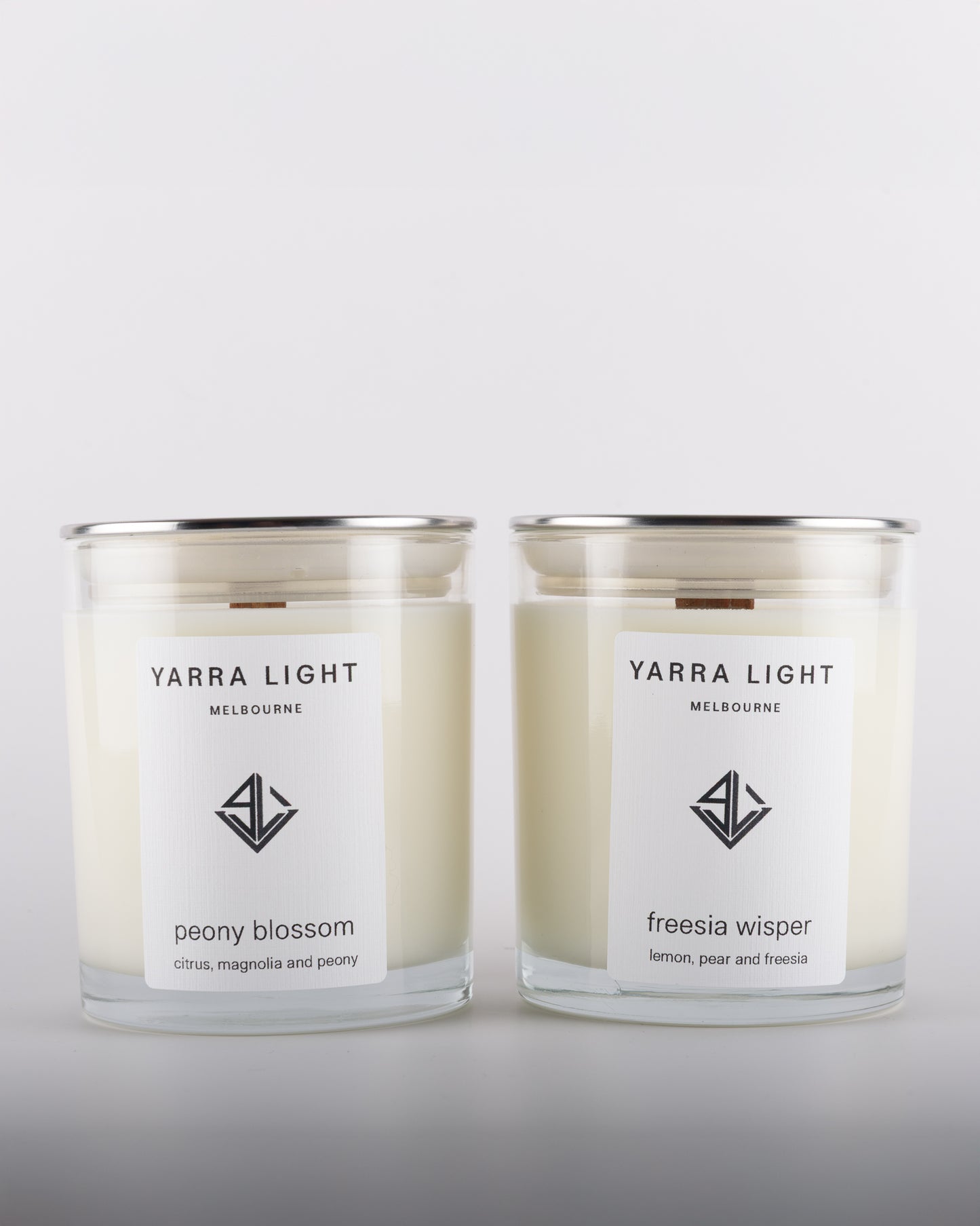 Bundle featuring Freesia Whisper and Peony Blossom soy wax scented candles with wood wicks in clear glass jars with minimalist labels, inspired by blooming freesia, sweet pear, and romantic peony fragrance notes.