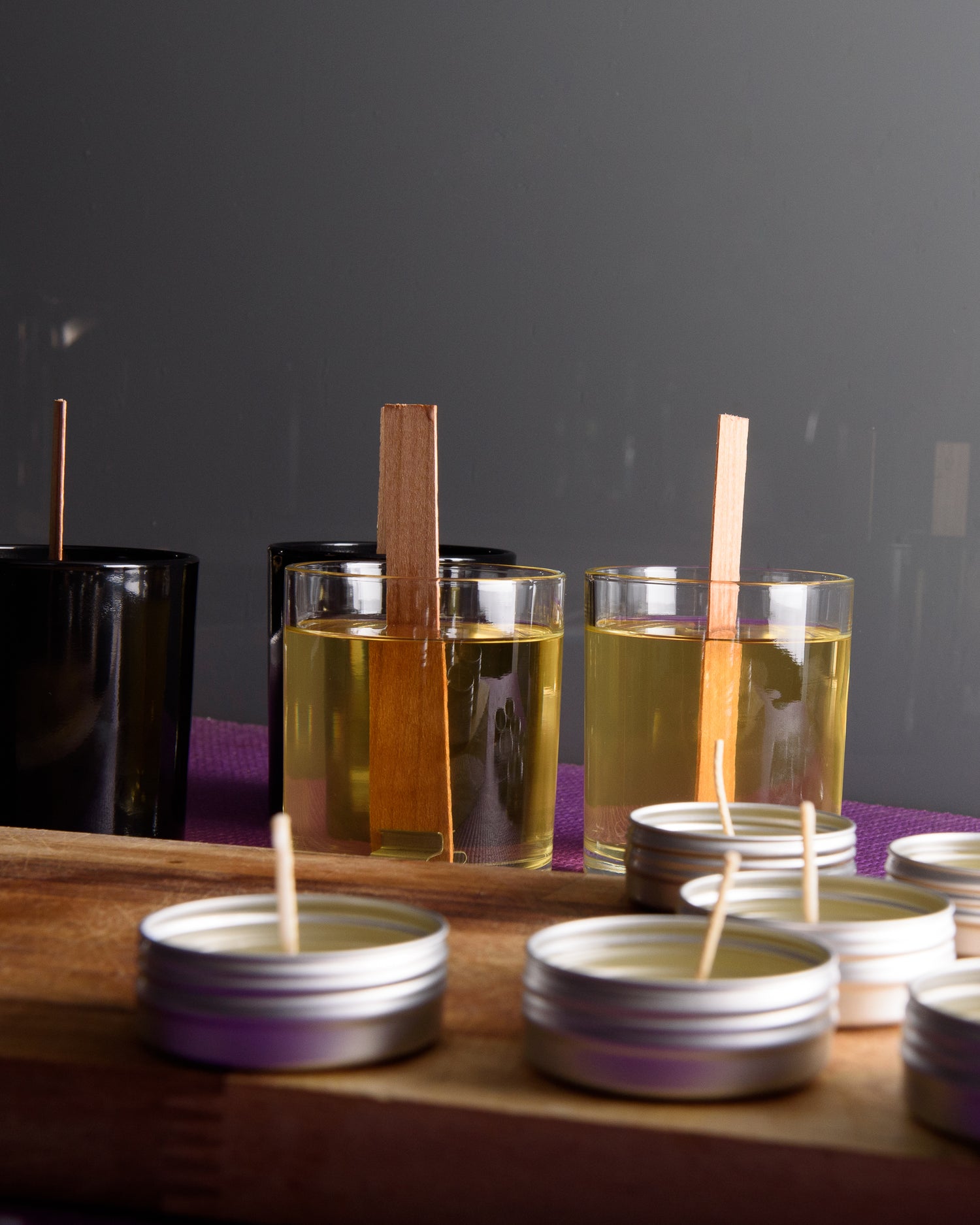 Candle-making setup with glass jars of liquid soy wax, wood wicks, and metal tins with cotton wicks